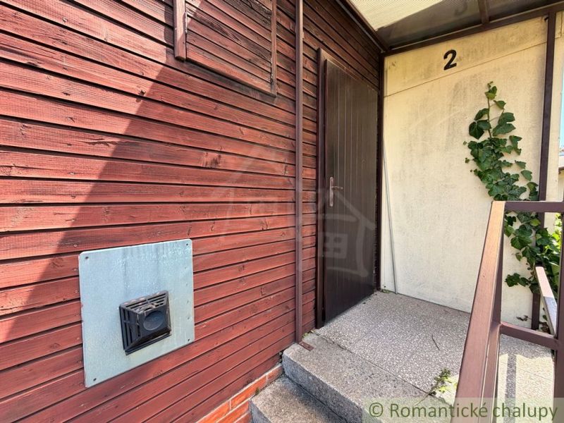 Eingang zur Holzhütte in Nové Zámky mit Kletterpflanzen an der Wand.