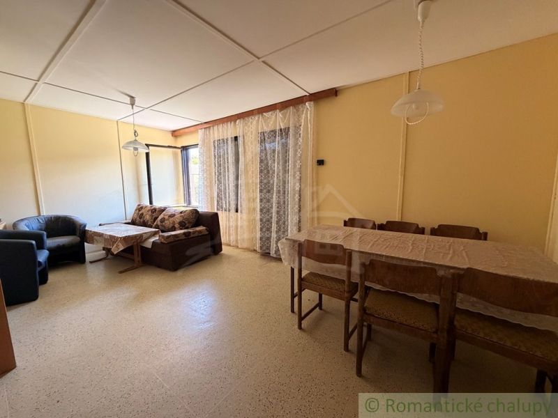 Das Innere der Hütte mit Esstisch, Sessel und Sofa neben Fenstern mit Spitze.
