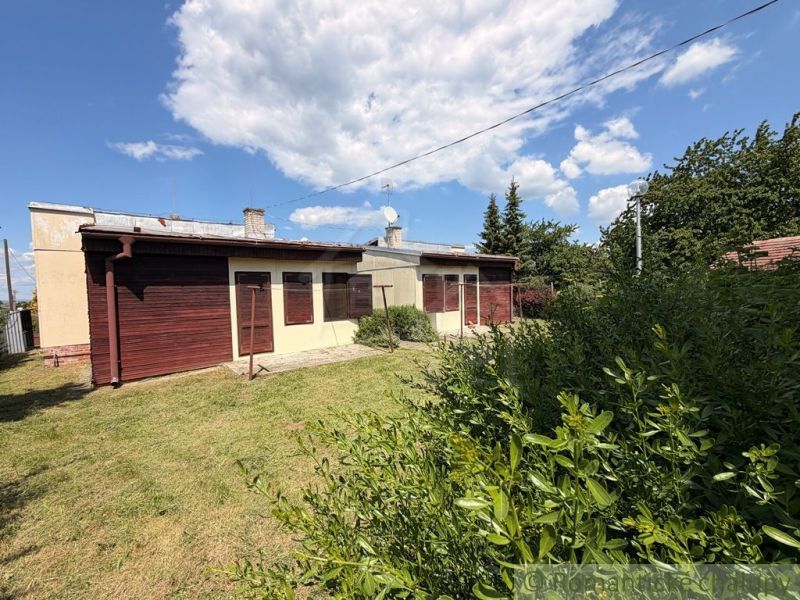 Ein Ferienhaus in Nové Zámky, umgeben von Rasen und Sträuchern unter blauem Himmel.