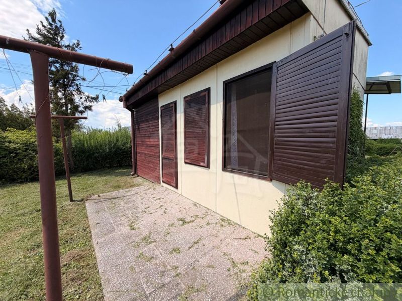Eine Hütte in Nové Zámky mit geschlossenen hölzernen Fensterläden und umgebendem Grün im Garten.