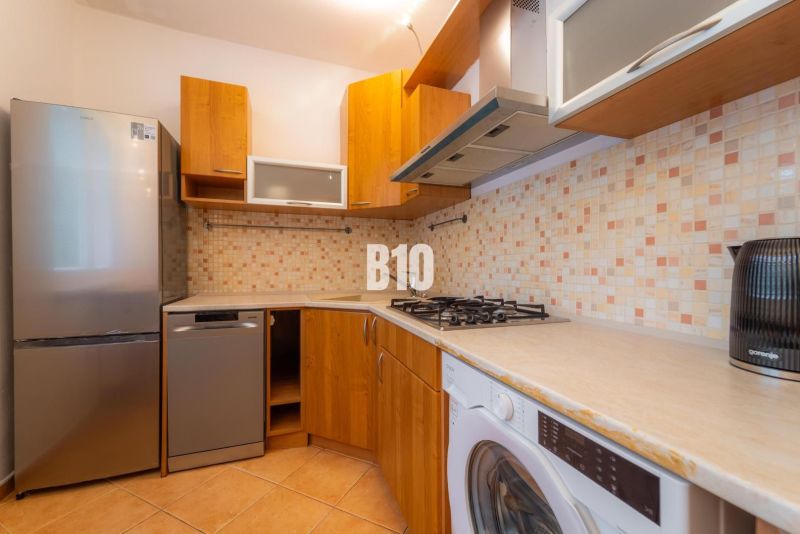 Küche mit gefliester Wand, Geräten und Holzboden in einer Zweizimmerwohnung.
