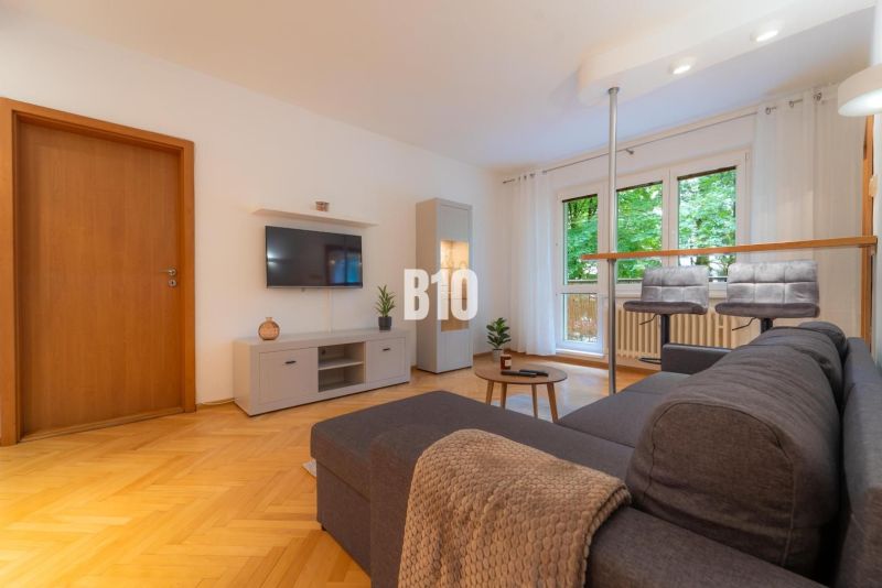 Wohnzimmer in einer 2-Zimmer-Wohnung mit Holzboden und Sitzgelegenheit am Fenster.