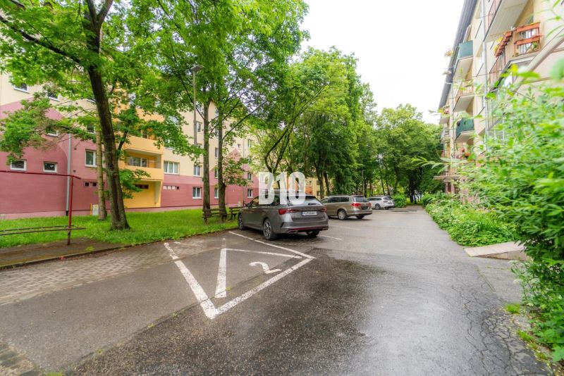 Ein Parkplatz mit Autos und Wohnhäusern, umgeben von Grünflächen in Martin.