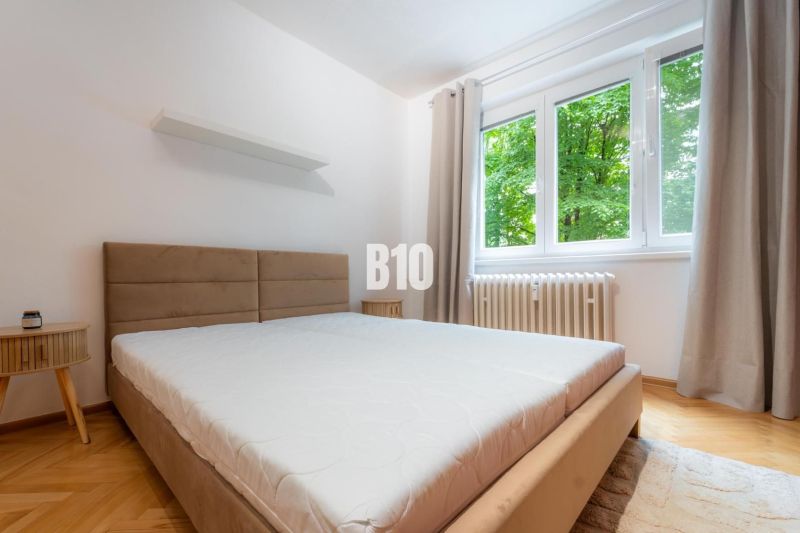 Schlafzimmer in einer 2-Zimmer-Wohnung mit großem Fenster und Boden in Holzoptik.