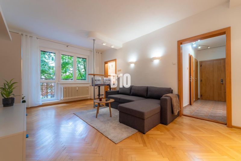 Wohnzimmer in einer Zweizimmerwohnung mit Holzboden und großem Fenster.