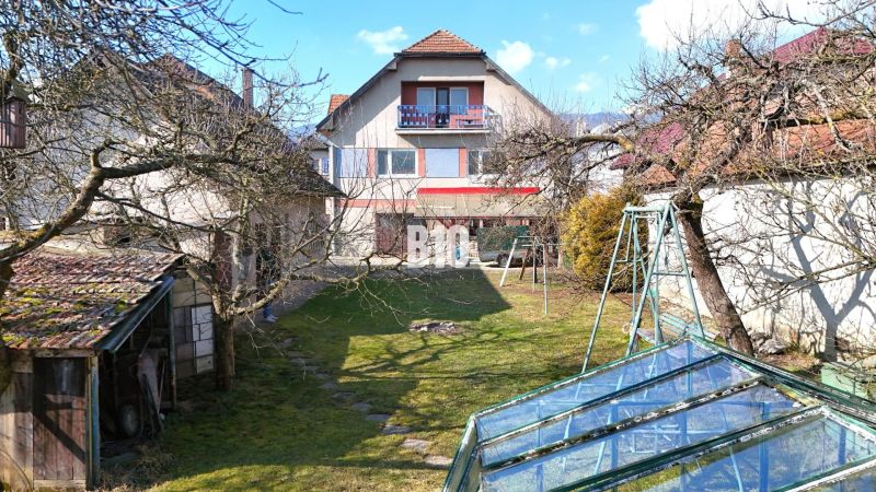 Ein Einfamilienhaus in Turany mit Rasen, Bäumen und einem Gewächshaus im Garten.