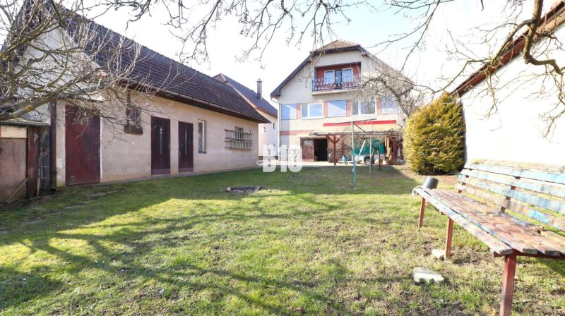 Ein Einfamilienhaus in Turany, umgeben von einem Garten mit einer Bank und Anbauten.