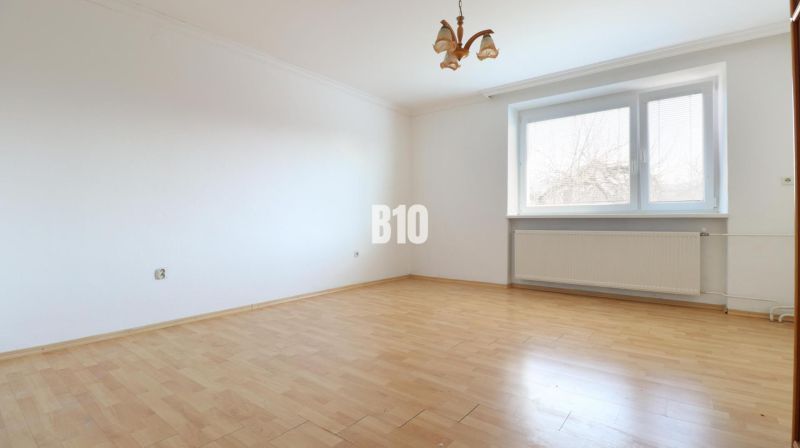 Ein geräumiges Zimmer mit weißen Wänden in einem Einfamilienhaus und einem Boden in Holzoptik.