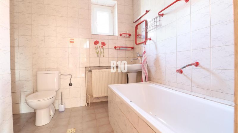 Badezimmer im Einfamilienhaus: Badewanne, Waschbecken, Toilette, weiße Fliesen mit roten Elementen.