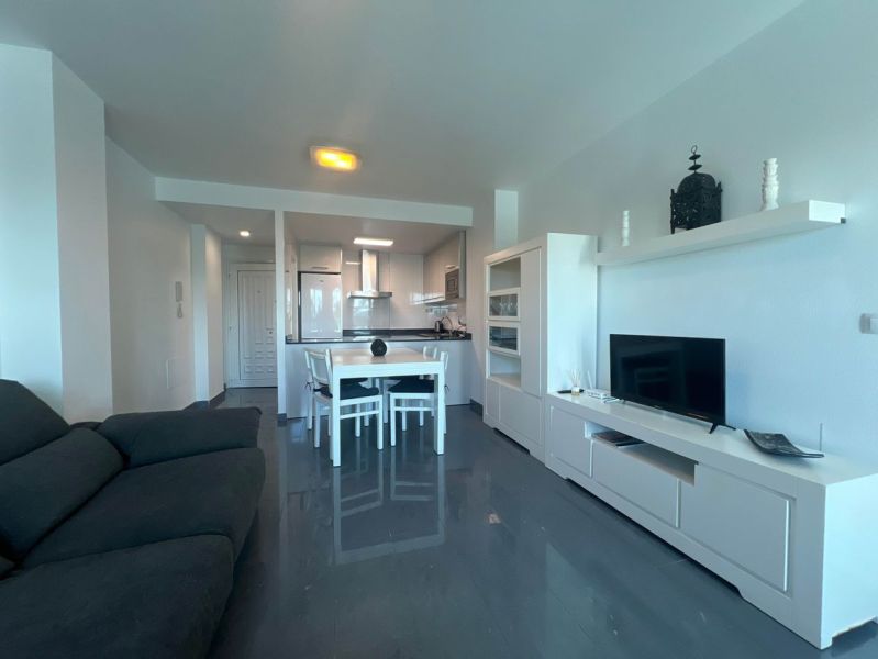 Ferienwohnung mit Sofa, Esstisch und Fernseher, Boden mit Holzdekor.