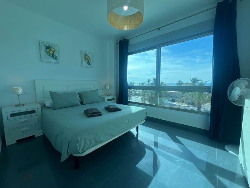 Schlafzimmer einer Ferienwohnung mit großem Fenster, Bett und Tischen.