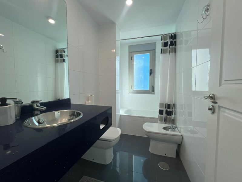 Badezimmer in einer Ferienwohnung mit Badewanne und Waschbecken auf einer dunklen Arbeitsplatte.