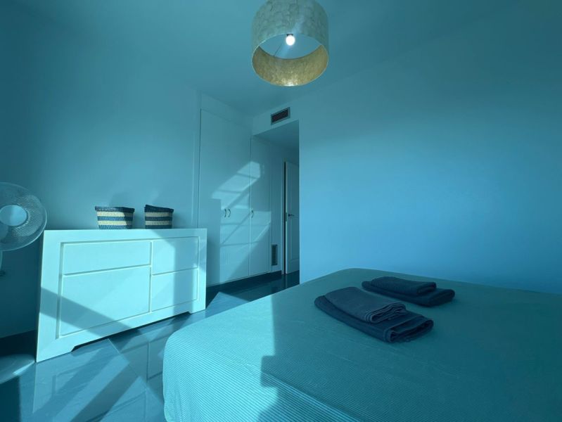 Ferienwohnung mit einem hellen Zimmer, Bett, Kommode und Loggia in blauen Tönen.