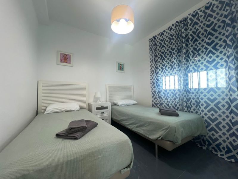 Ferienwohnung mit zwei Einzelbetten, gemusterten Vorhängen und einem Tisch mit Lampe.