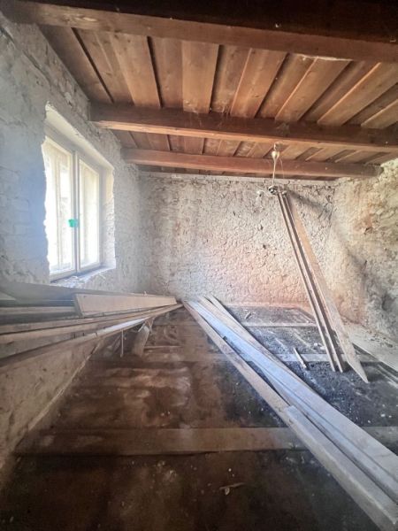 Ein Zimmer in einem Einfamilienhaus mit Steinwänden und einer Holzdecke, Material auf dem Boden.