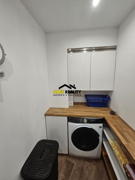 Waschküche in einer 3-Zimmer-Wohnung mit Waschmaschine, Stauraum und einem Boden in Holzoptik.