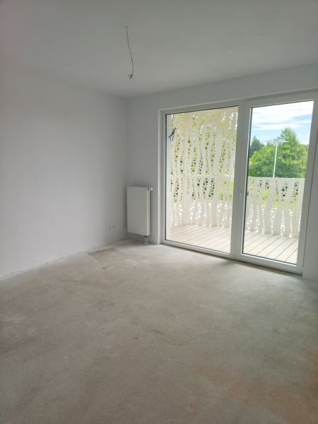 Ein Zimmer in einer 2-Zimmer-Wohnung mit Balkon, großem Fenster und Heizkörper an der Wand.