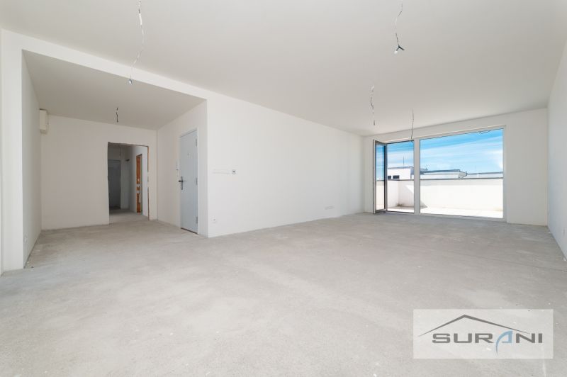 Ein leerer Raum in einer 3-Zimmer-Wohnung mit einem großen Fenster und einer Terrasse.