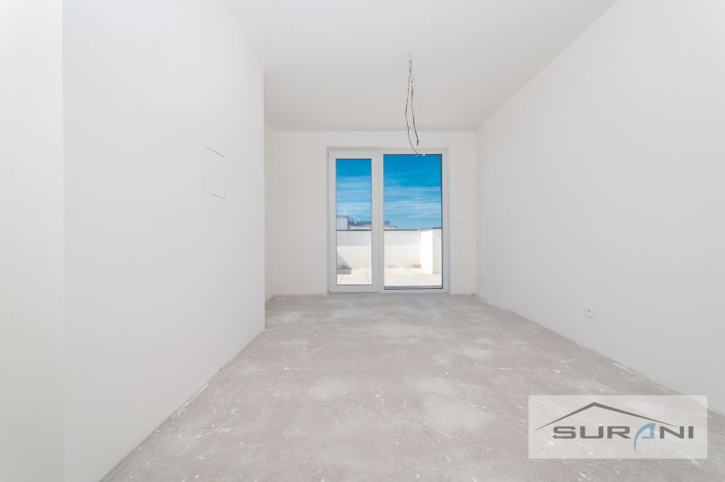 Ein leerer Raum mit Betonboden und Balkontüren in einer 3-Zimmer-Wohnung.