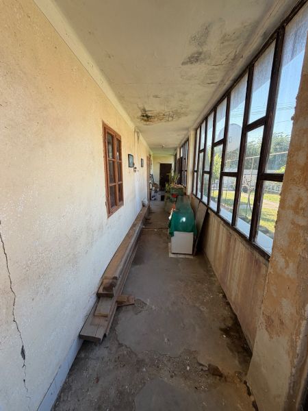Ein schmaler Gang auf der Veranda in einem Einfamilienhaus mit alten Fenstern und rissigen Wänden.