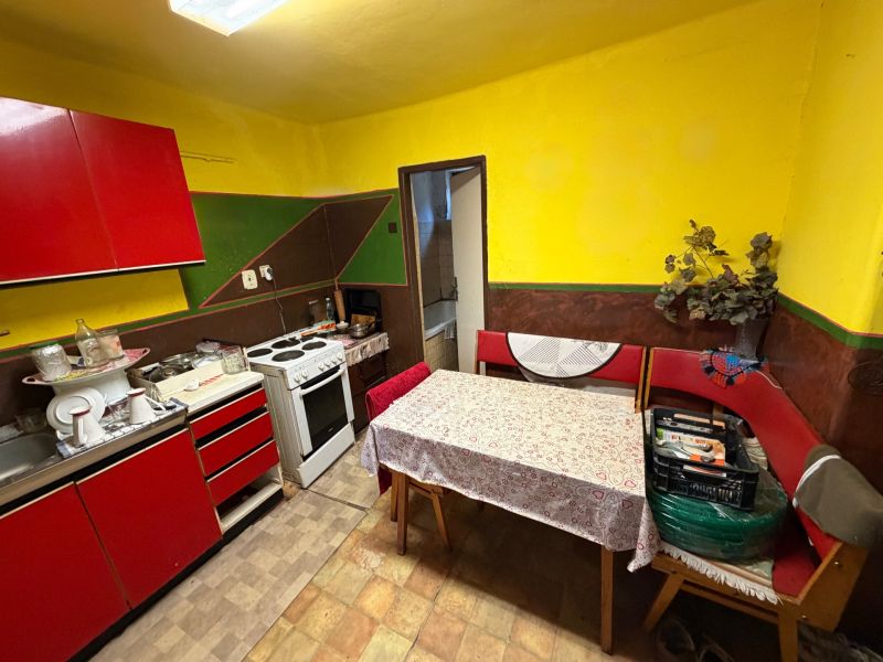 Eine Küche in einem Einfamilienhaus mit roten Möbeln, einem Tisch und einem Elektroherd.