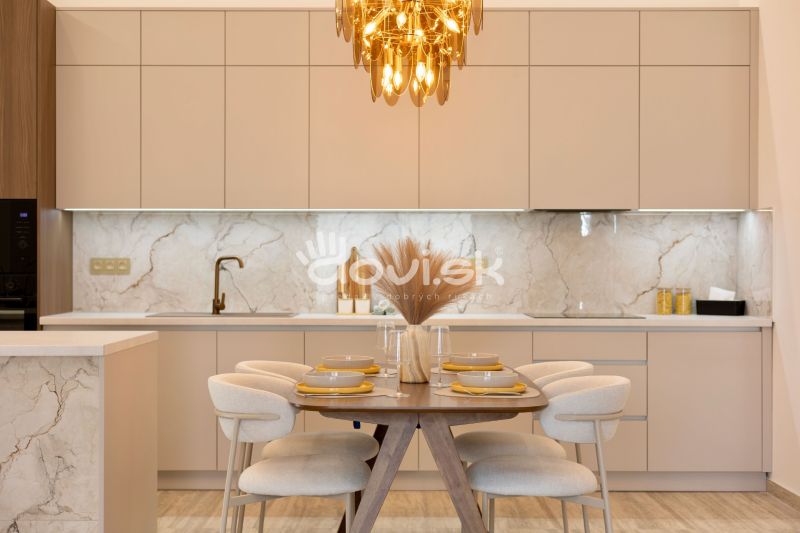 Küchenbereich mit Esstisch, beige Schränke, Boden mit Holzdekor, Leuchte.
