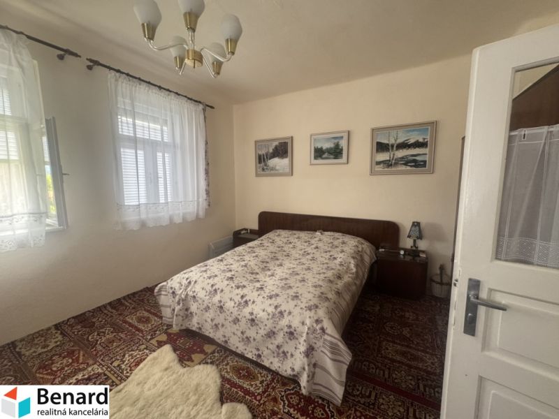 Schlafzimmer im Einfamilienhaus mit Bett, Teppich und Vorhängen an den Fenstern.