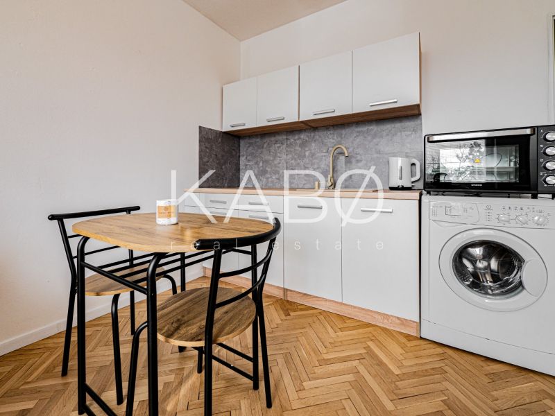 Einzimmerwohnung mit Küchenzeile und Geräten, Boden mit Holzdekor, Esstisch und Stühle.