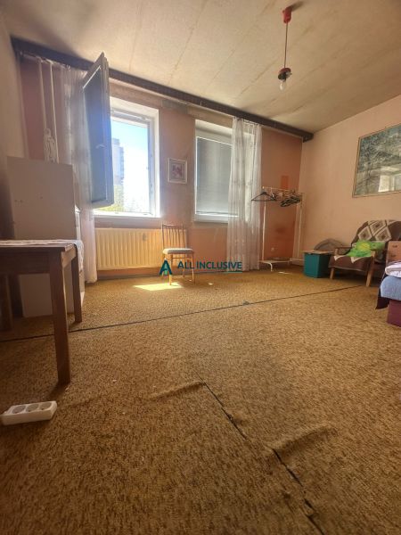 Ein Zimmer in einer 2-Zimmer-Wohnung mit Teppich, offenem Fenster und einfacher Einrichtung.