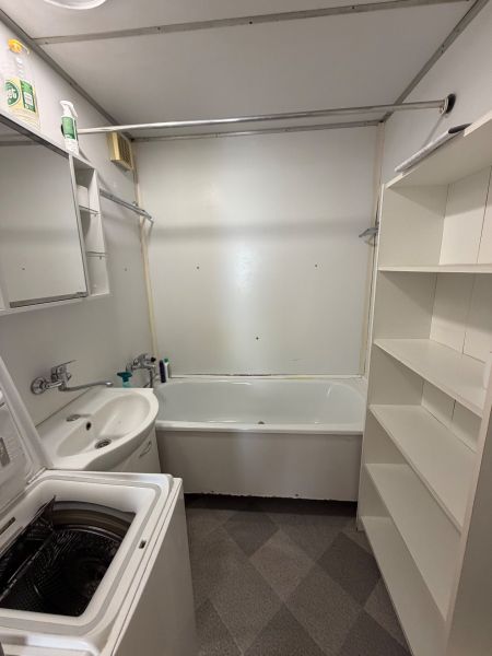 Badezimmer in einer 3-Zimmer-Wohnung mit Badewanne, Waschbecken, Waschmaschine und Regalschrank.