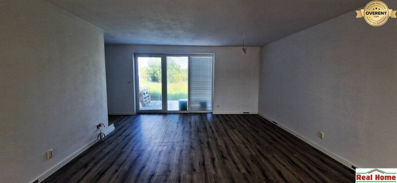 Ein Zimmer in einem Einfamilienhaus, große Fenster, weiße Wände, Holzboden.