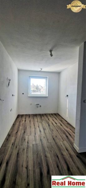Ein Blick in einen Raum eines Einfamilienhauses mit einem Boden in Holzoptik und einem Fenster.
