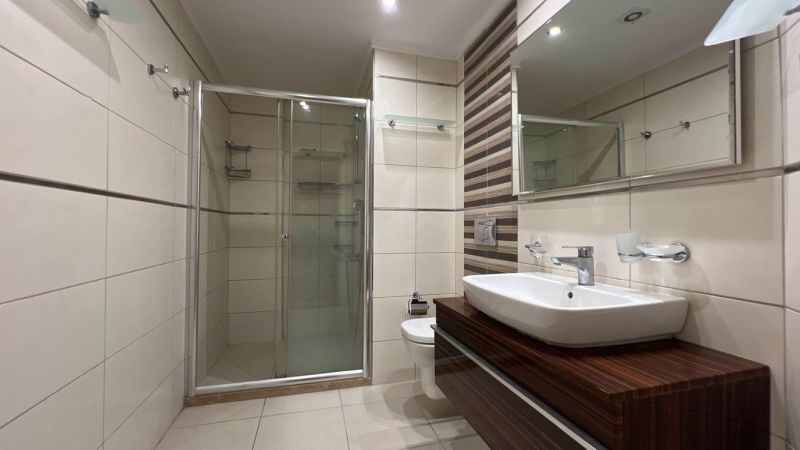 Badezimmer mit Dusche, Waschbecken und Schränken mit Holzdekor auf Besonderen Immobilien.