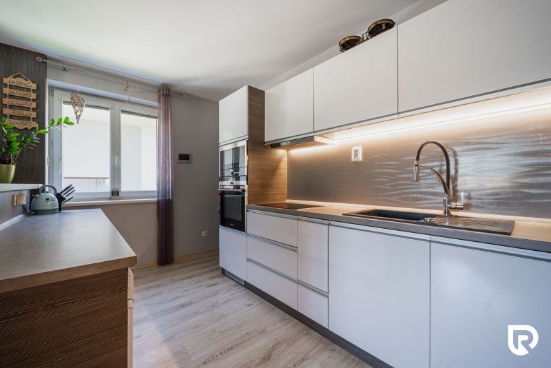 Eine Küche in einem Einfamilienhaus mit weißen Schränken, einem Boden in Holzoptik und einem Fenster.