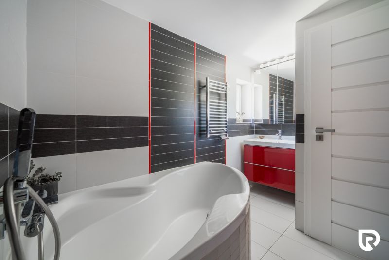 Badezimmer in einem Einfamilienhaus mit Badewanne, rotem Schrank und silbernem Heizkörper.