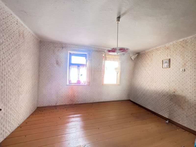 Ein leerer Raum in einem Einfamilienhaus mit Holzboden und einem Blumenleuchter.