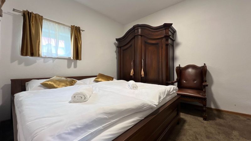 Schlafzimmer in der Villa mit Schrank, Sessel, Bett und goldenen Kissen.