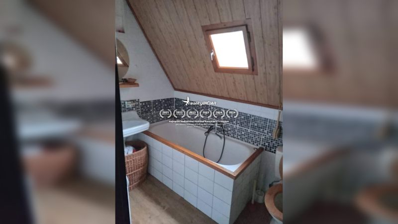Badezimmer mit Badewanne und schräger Decke, Holzelemente, Mosaikfliesen, Fenster.