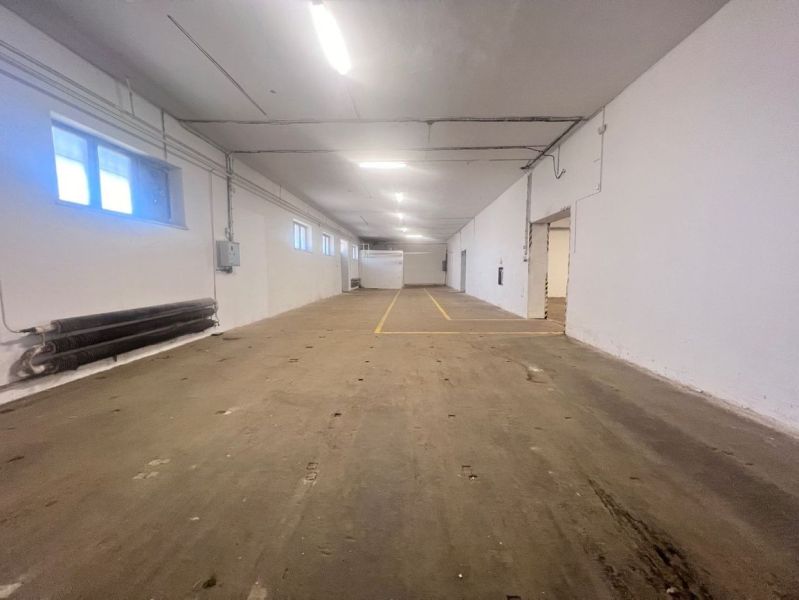 Innenraum eines Lagers mit Betonboden und weißen Wänden, Leuchtstoffbeleuchtung.