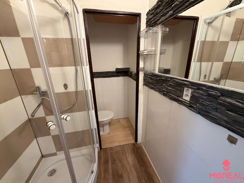 Kompaktes Badezimmer in einer Einzimmerwohnung mit Holzboden und Duschkabine.