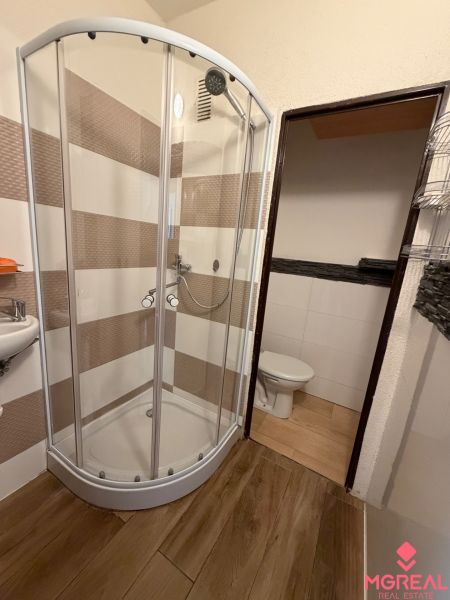 Duschkabine und Boden mit Holzdekor im Badezimmer einer Einzimmerwohnung.