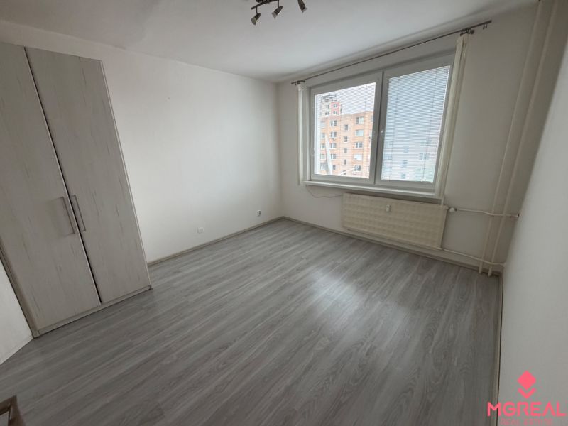 Ein Zimmer in einer Einzimmerwohnung mit einem Boden in Holzoptik und weißen Wänden.
