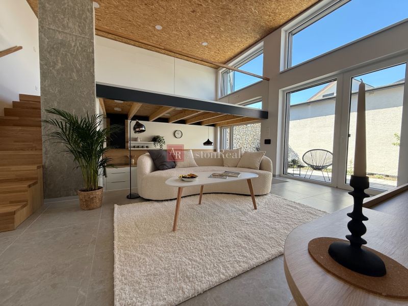 Wohnbereich in einem Einfamilienhaus mit Treppe, Sofa und großen Fenstern zur Terrasse.