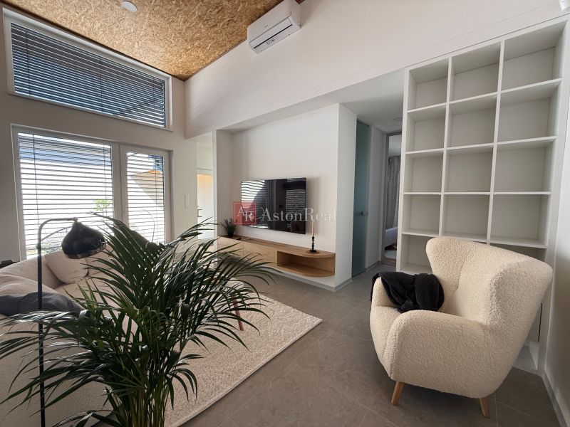 Wohnzimmer in einem Einfamilienhaus mit einem cremefarbenen Sessel und einem Fernseher, Boden mit Holzdekor.