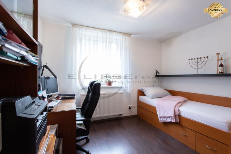 Ein Zimmer in einem Einfamilienhaus mit einem Bett, einem Schreibtisch und einem Boden mit Holzdekor.