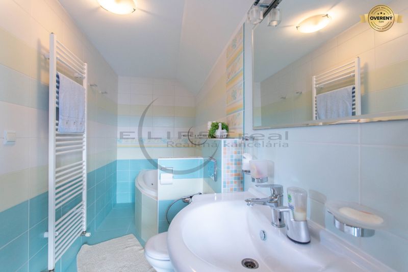 Ein Badezimmer in einem Einfamilienhaus mit einem weißen Waschbecken, einer Badewanne, einem Spiegel und einem Handtuchhalter.