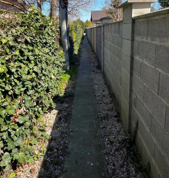 Ein schmaler Gehweg an der Mauer zwischen Blumen und Zaun in der Hrušovská in Bratislava, Stadtteil Vrakuňa, Grundstücke - Wohnen.