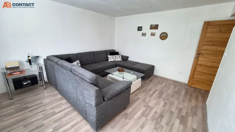 Wohnzimmer mit Ecksofa, Glastisch und Boden in Holzoptik.