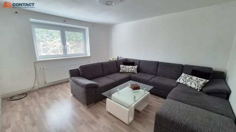 Wohnzimmer mit einer grauen Eckcouch und einem Tisch, Holzboden mit Holzdekor.