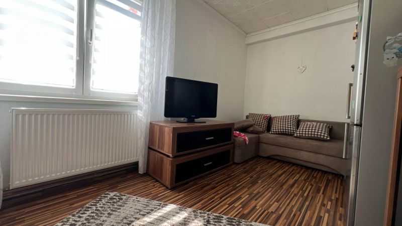 Wohnzimmer mit Holzboden, Sofa, Fernseher und Heizkörper in einer 3-Zimmer-Wohnung.
